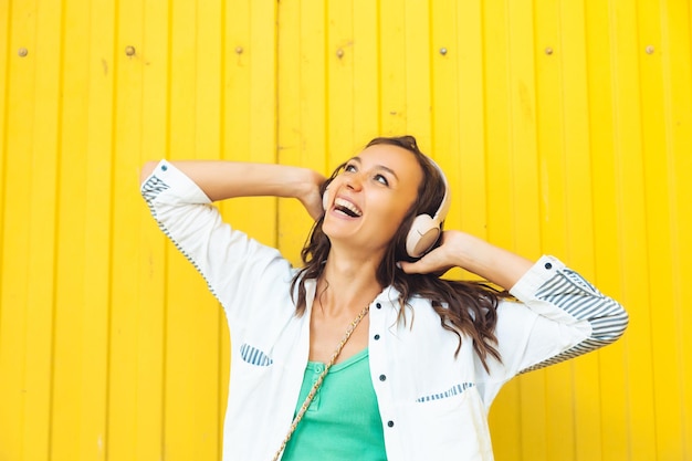 A fulllength view of a beautiful cheerful girl jumping while listening to a melody isolated against a bright yellow background a young woman with headphones dancing on the street generation z