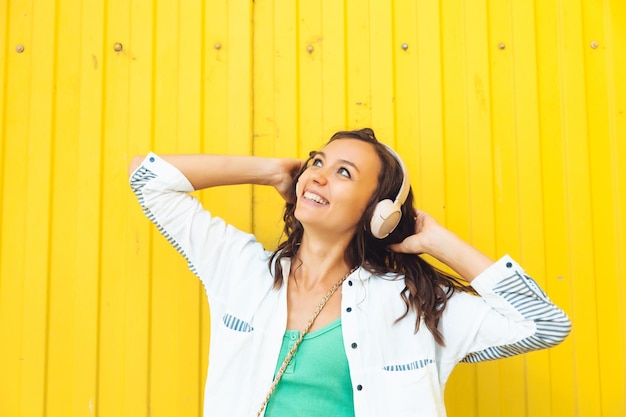 A fulllength view of a beautiful cheerful girl jumping while listening to a melody isolated against a bright yellow background a young woman with headphones dancing on the street generation z