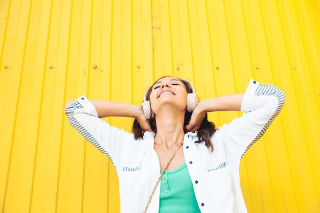 A fulllength view of a beautiful cheerful girl jumping while listening to a melody isolated against a bright yellow background a young woman with headphones dancing on the street generation z