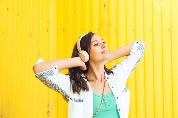 A fulllength view of a beautiful cheerful girl jumping while listening to a melody isolated against a bright yellow background a young woman with headphones dancing on the street generation z