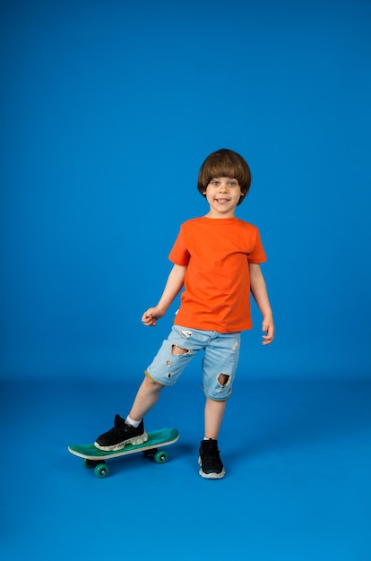 Fun caucasian toddler is playing with a skateboard on a blue surface with space for text. Vertical orientation