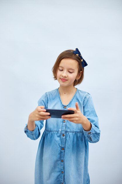 Fun excited kid girl in casual denim dress use with smartphone