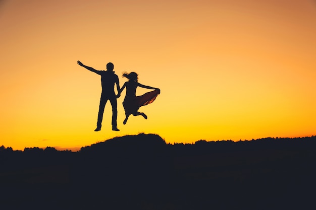 Fun loving couple jumping at sunset, silhouette