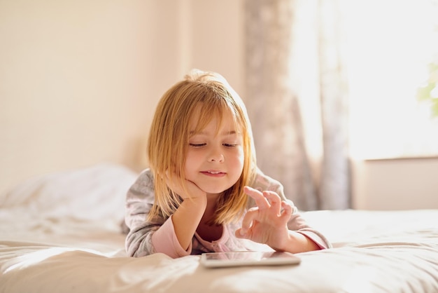 Fun online anytime Shot of a little girl playing with her tablet while lying on her bed at home