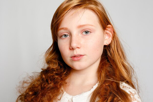 Fun Portrait of an Adorable Red Haired Girl on a Grey Background. Beauty, kid fashion, cosmetics, healthy hair. Hairdresser, makeup, shampoo.