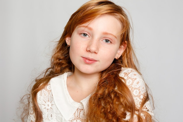 Fun Portrait of an Adorable Red Haired Girl on a Grey Background. Beauty, kid fashion, cosmetics, healthy hair. Hairdresser, makeup, shampoo.