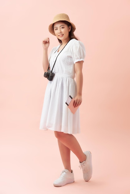 Fun travel portrait of smiling young beautiful Asian tourist woman holding passport isolated on pink background