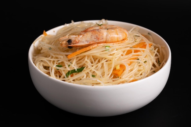 Funchosa salad with shrimps in a white bowl on a black background