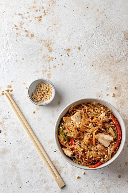 Funchose salad with chicken and vegetables in bowl with wooden chopsticks Top view