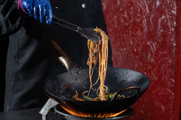 Funchoza flambe rice noodles with vegetables cooking on fire in wok pan. Street food.