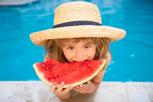 Funny amazed child eats watermelon near the pool