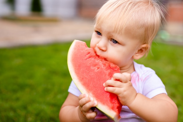 Funny baby eating watermelon outdoors in the park. Baby, baby, healthy food