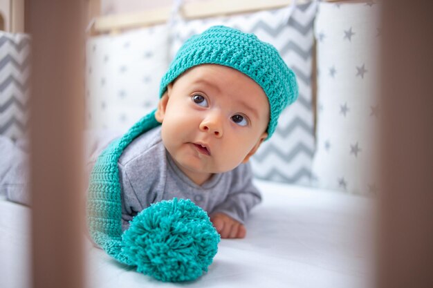 A funny baby in a funny hat lies on his stomach with his head raised