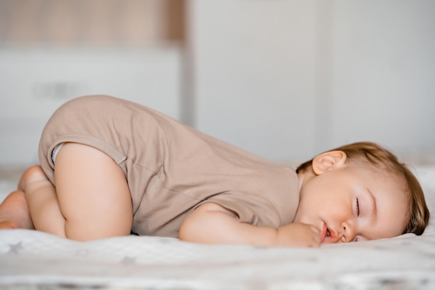 Funny baby with open mouth sleeping on his stomach on the bed at home