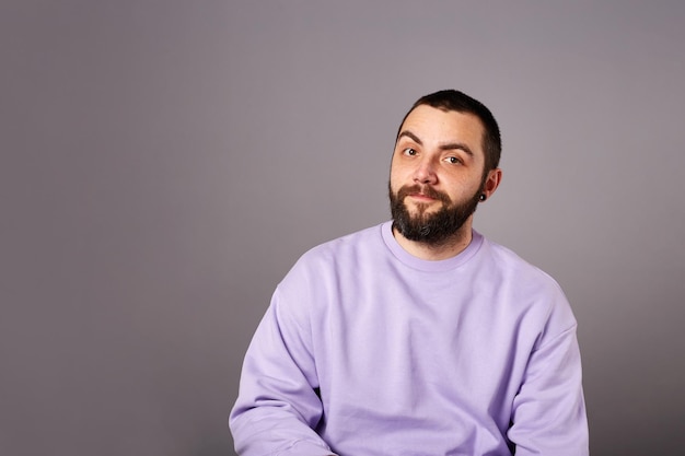 Funny bearded man wears violet sweater on grey background Copy space