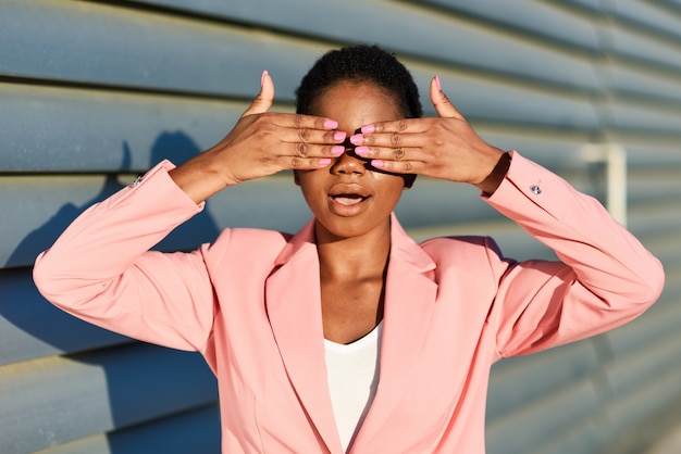 Funny black woman standing on urban wall covering her eyes with her hands