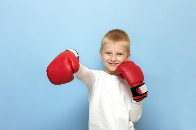 Funny blond boy in red boxing gloves depicts a boxer