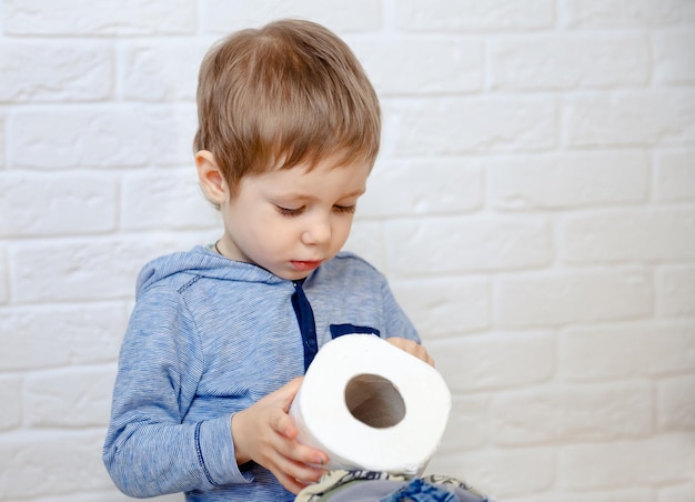 Funny boy sitting on potty chair and playing with toilet paper