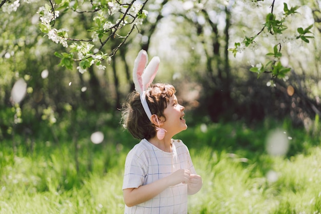 Funny boy with eggs basket and bunny ears on easter egg hunt in sunny spring garden