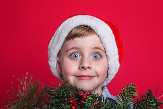 Funny boy with Santa Claus hat on red background.