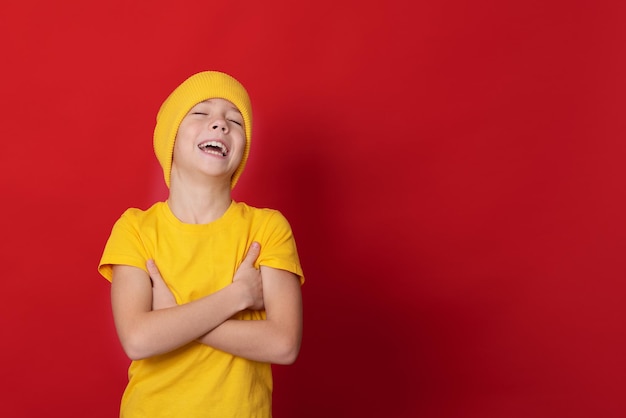 funny boy in a yellow tshirt and cap is making faces on the red background