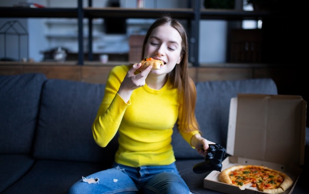 Funny brunette girl in yellow sweater eating pizza at home