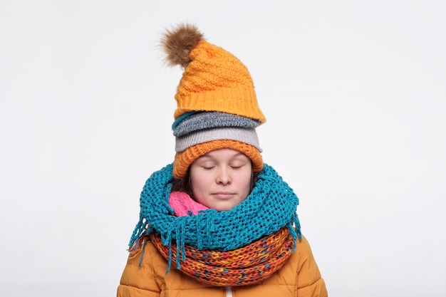 Funny caucasian female teenager in several scarfs and hats relaxing with closed eyes.