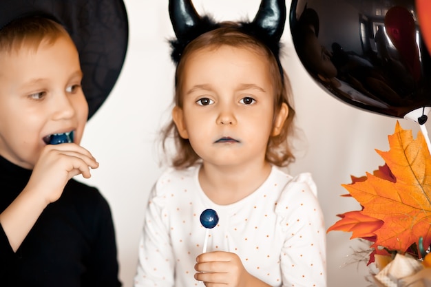 Funny child girl and boy in witch and evil costumes for Halloween eating candies lolly pops and have fun.