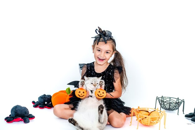 Photo funny child girl in a witch costume for halloween with a cat in a suit in her hands