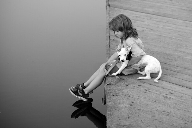 Funny child playing with her puppy dog in the park near lake carefree childhood protection domestic