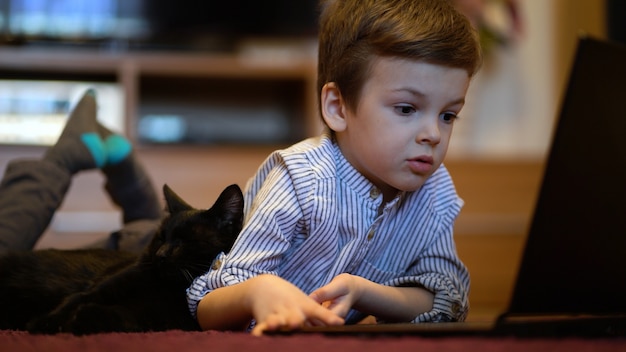 Funny child with kitten using a laptop at home