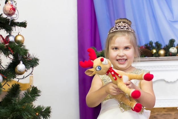 Funny child with a toy by the Christmas tree in kindergarten