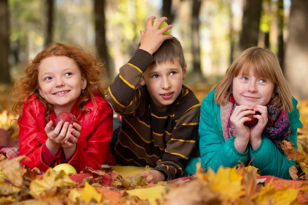 Funny children boy and girls lie on maple leaves in the autumn park