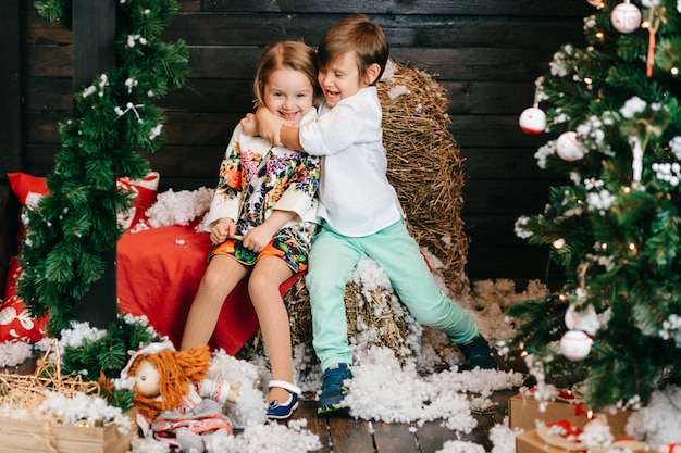 Funny children hugging in studio with christmas tree and new year decorations.