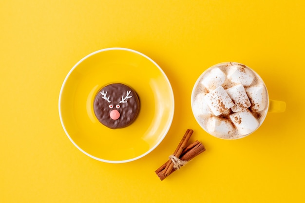 Funny Christmas chocolate reindeer cookie on cup saucer and a coffee with marshmallow on yellow