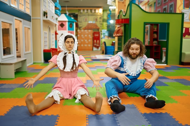 Funny comic man and woman wearing like newborn babies sitting on playroom floor