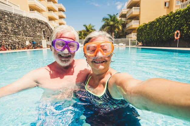 Funny couple of mature people take selfie picutre while enojy and have fun at the pool in residence - elderly retired happy lifestyle with aged couple in summer leisure activity together