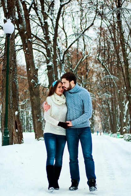 funny couple. snowy park. young man, woman near snow covered pine trees. warm sweaters. Family, love