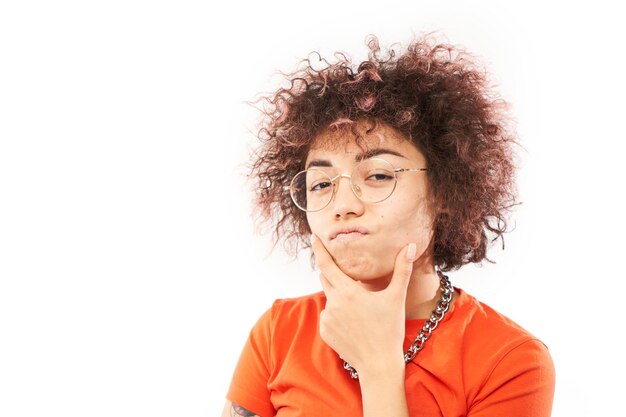 Funny curly girl holding her chin thinks doubts makes decision isolated on white studio background