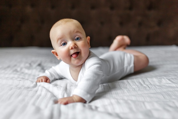 Funny cute baby in a white light bodysuit on the bed at home looking