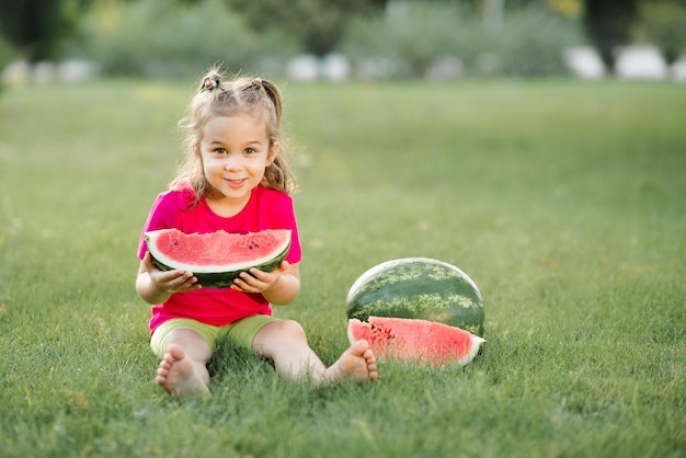 Funny cute child girl 3-4 year old eating ripe watermelon on green grass outdoor