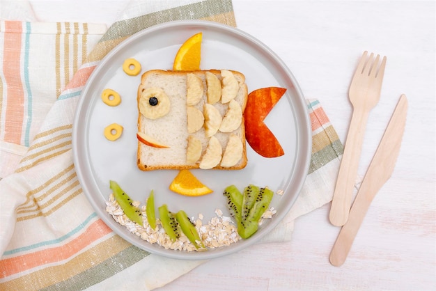 Funny cute fish shape sandwich toast bread with banana appleorange Kids childrens baby's sweet dessert healthy breakfast lunch food art on platewooden background close uptop view