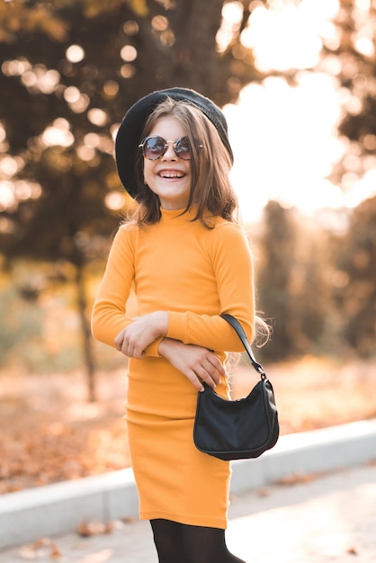 Funny cute kid girl 4-5 year old wear sun glasses and yellow knitted dress posing over nature autumn