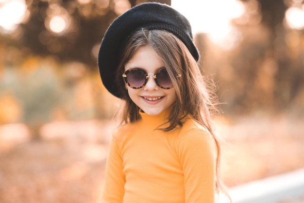 Funny cute kid girl 4-5 year old wear sun glasses and yellow knitted dress posing over nature autumn