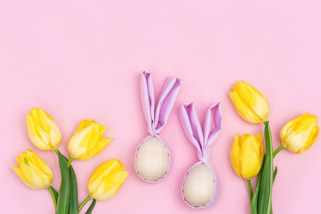 Funny Easter concept, yellow flowers tulip and wooden easter eggs with fabric ears as fun bunny