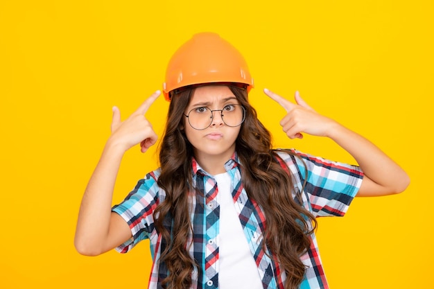 Funny face Child builder in helmet Teenage girl painter with painting brush tool or paint roller Child on repairing work isolated on yellow background Kids renovation concept