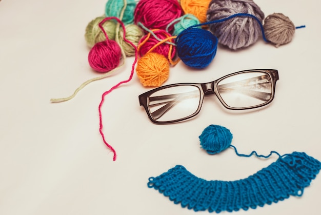 Funny face made of multicolored clews and glasses on white background.