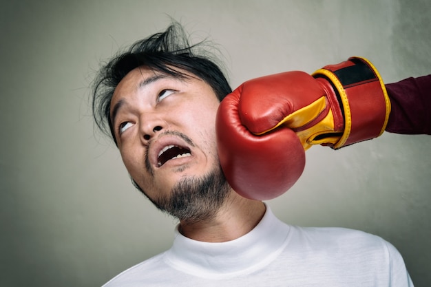 funny face man getting punch in face with boxing glove against gray background