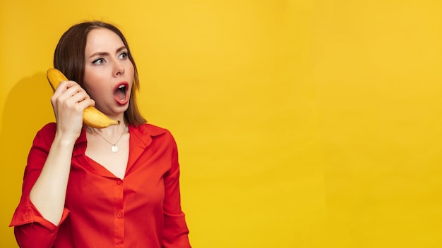 Funny face with a banana A young woman with a smile holds a banana in her hand Funny expressions The concept of nutrition Fresh banana Yellow style Vitamins Empty space for your text or advertisement