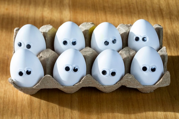 Funny faces on white eggs in carton box with organic chicken eggs on kitchen table closeup big animation eyes humor food and easter holiday concept